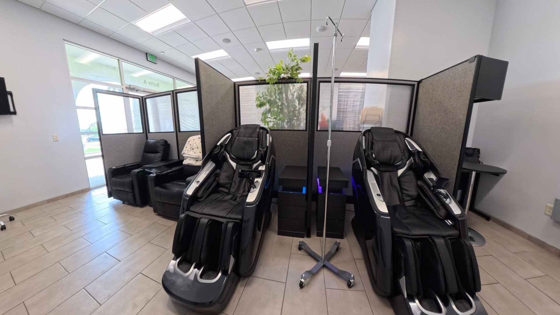 The clinic’s two black multi-zone massage chairs beside IV poles and privacy dividers